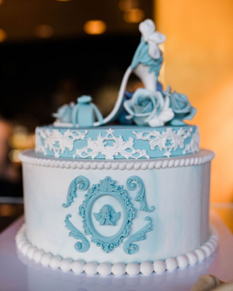 Custom celebration cake in white and pale blue with a sugar slipper on top