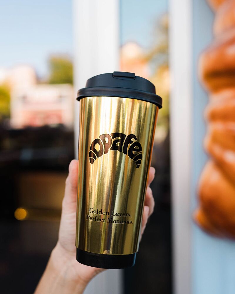 Gold Opafe tumbler held up beside an oversized croissant